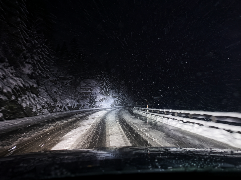 Nachtfahrt auf einer verschneiten Alpenstrasse mit Schneematsch, starkem Schneefall und winterlichen Fahrbedingungen.