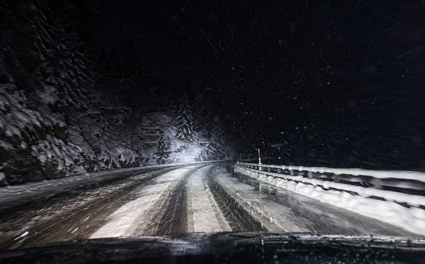 Nachtfahrt auf einer verschneiten Alpenstrasse mit Schneematsch, starkem Schneefall und winterlichen Fahrbedingungen.