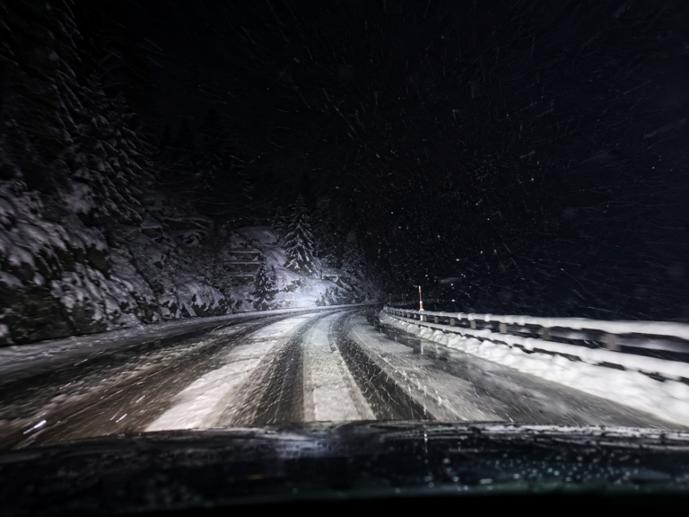 Nachtfahrt auf einer verschneiten Alpenstrasse mit Schneematsch, starkem Schneefall und winterlichen Fahrbedingungen.