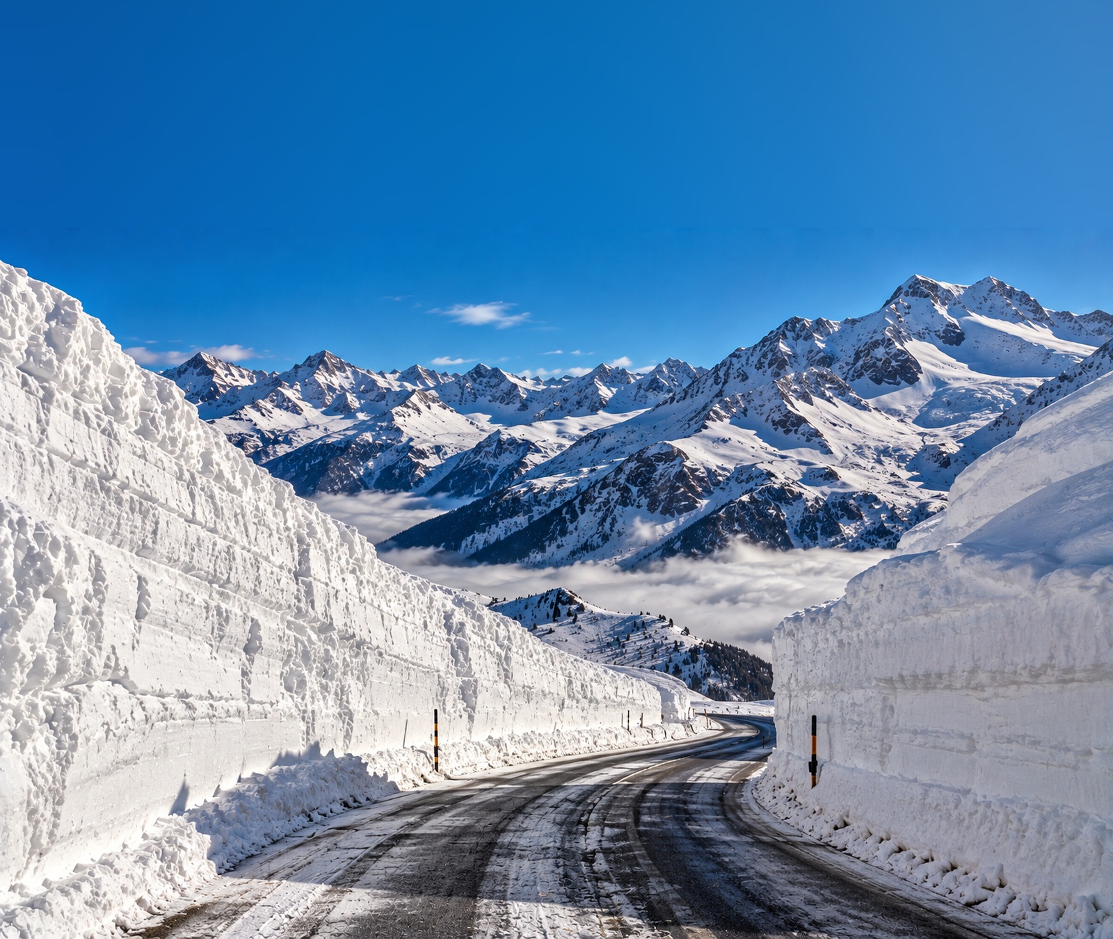 Symbolbild einer geräumten hochalpinen Passstrasse zwischen meterhohen Schneewänden