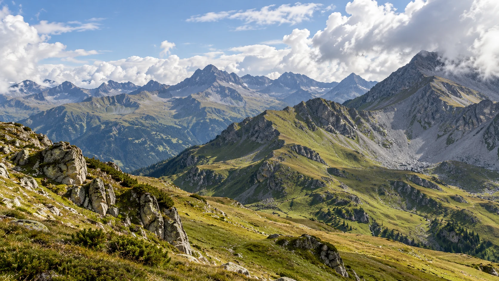 Spätsommerliche Alpenlandschaft mit Gras, Geröll und hohen Gipfeln unter blauem Himmel.