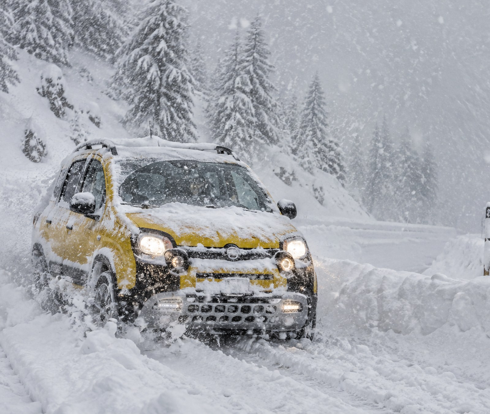 Gelber Fiat Panda Cross auf einer tief verschneiten Alpenstrasse bei extrem dichtem Schneefall.