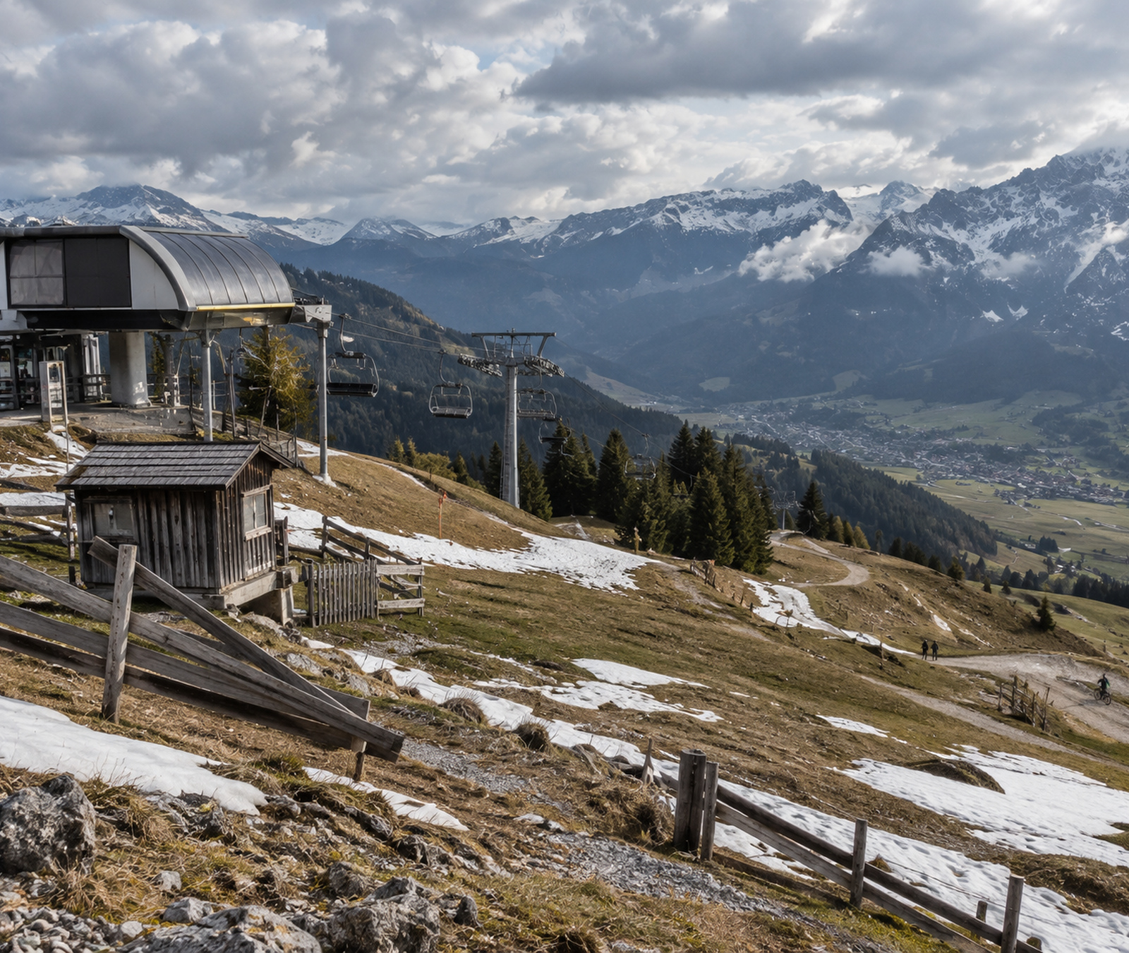 Kleines geschlossenes Skigebiet in den Alpen mit stillstehendem Sessellift, schneearmen Hängen und Wanderwegen
